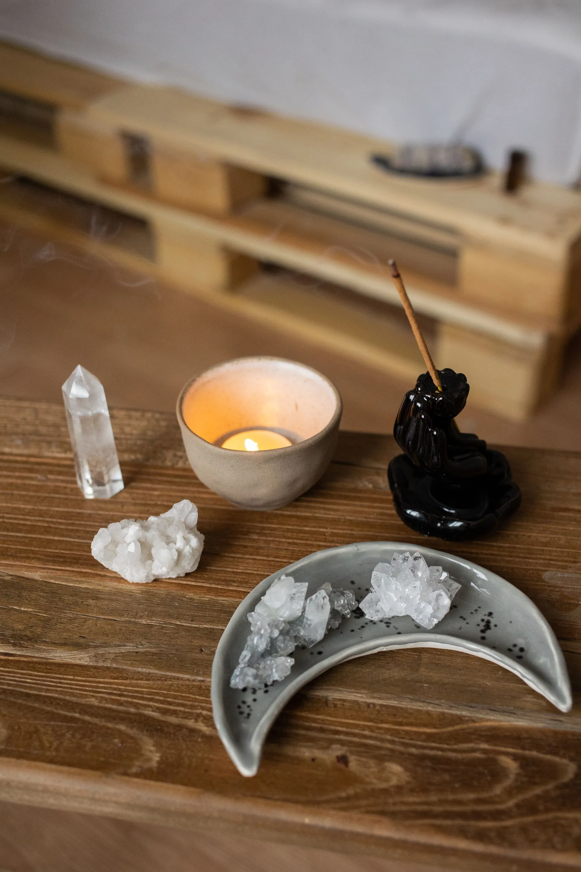 A lit candle, incense and clear crystals on a wooden table
