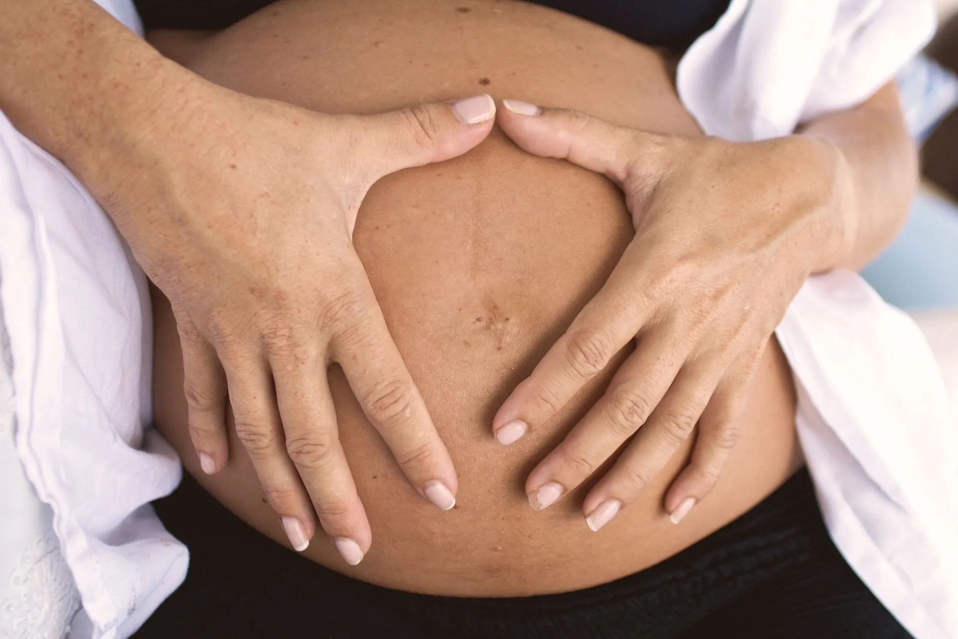 Hands forming a heart shape on a pregnant belly