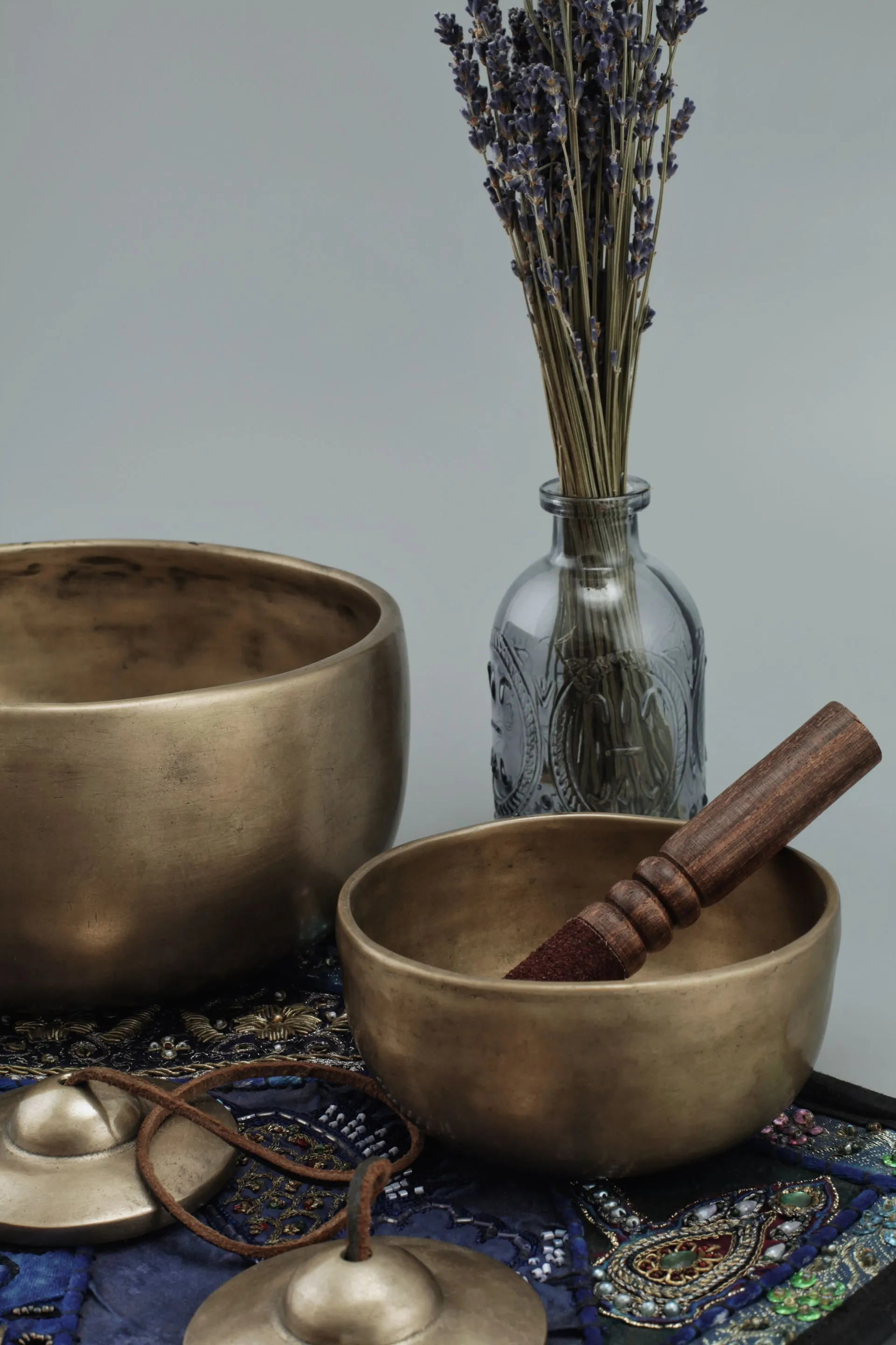 Two brass singing bowls and a wooden mallet beside a vase of dried lavender